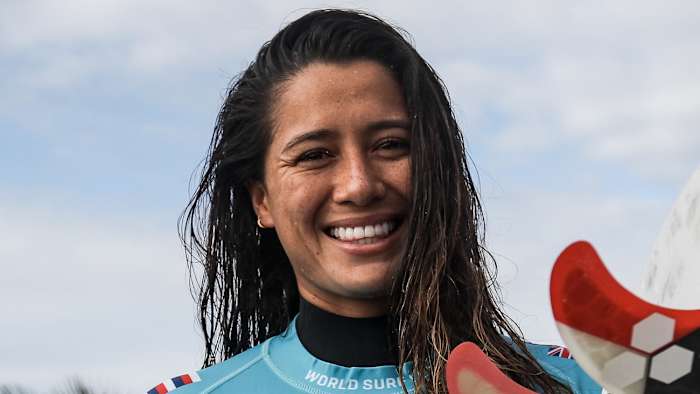 Malia Manuel poses in a blue surf shirt and wet hair and smiles at the camera.